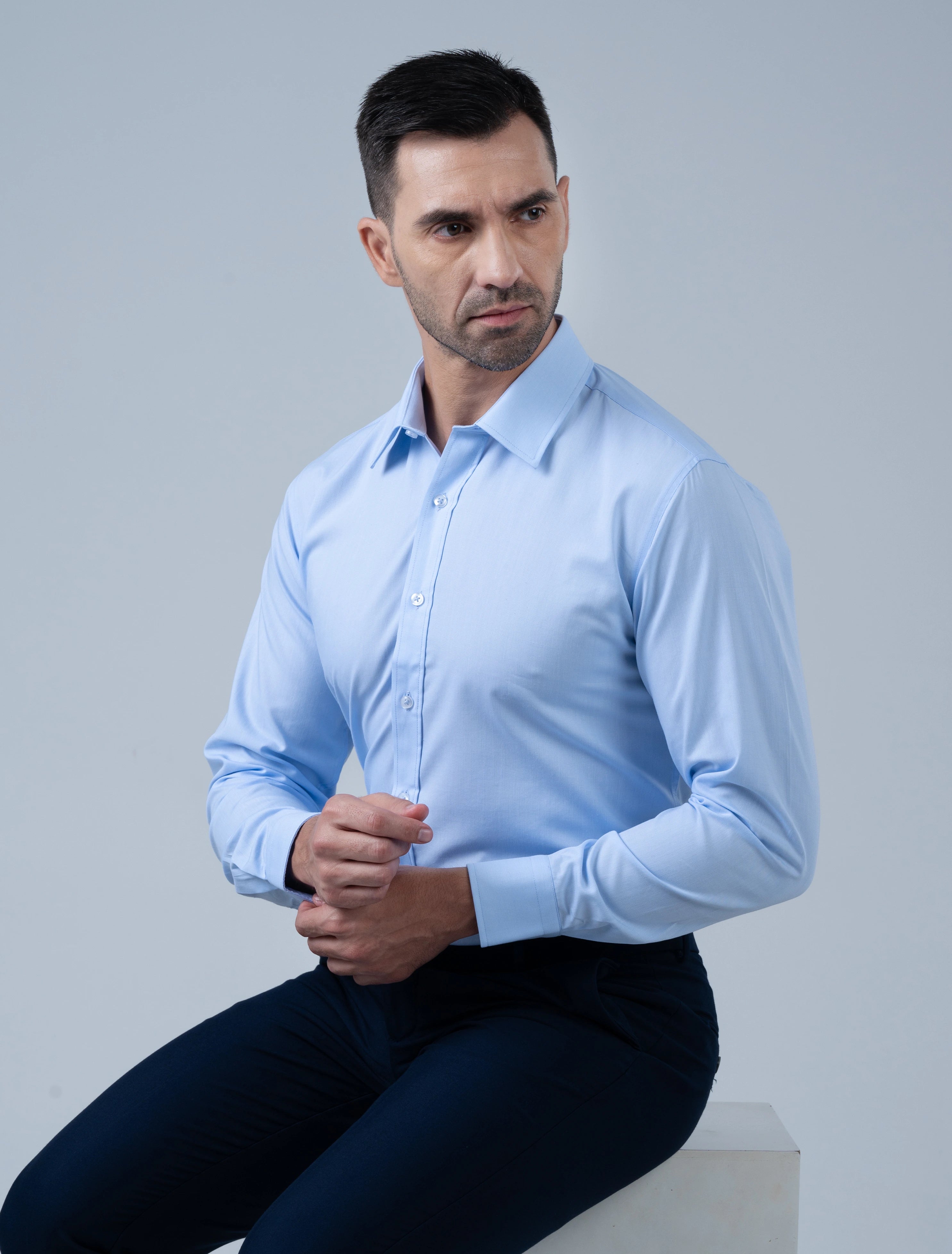 Model seated wearing the Marshall Menswear Kingsley premium men's business casual shirt in light blue with a tailored fit, crisp collar and refined office-ready style.