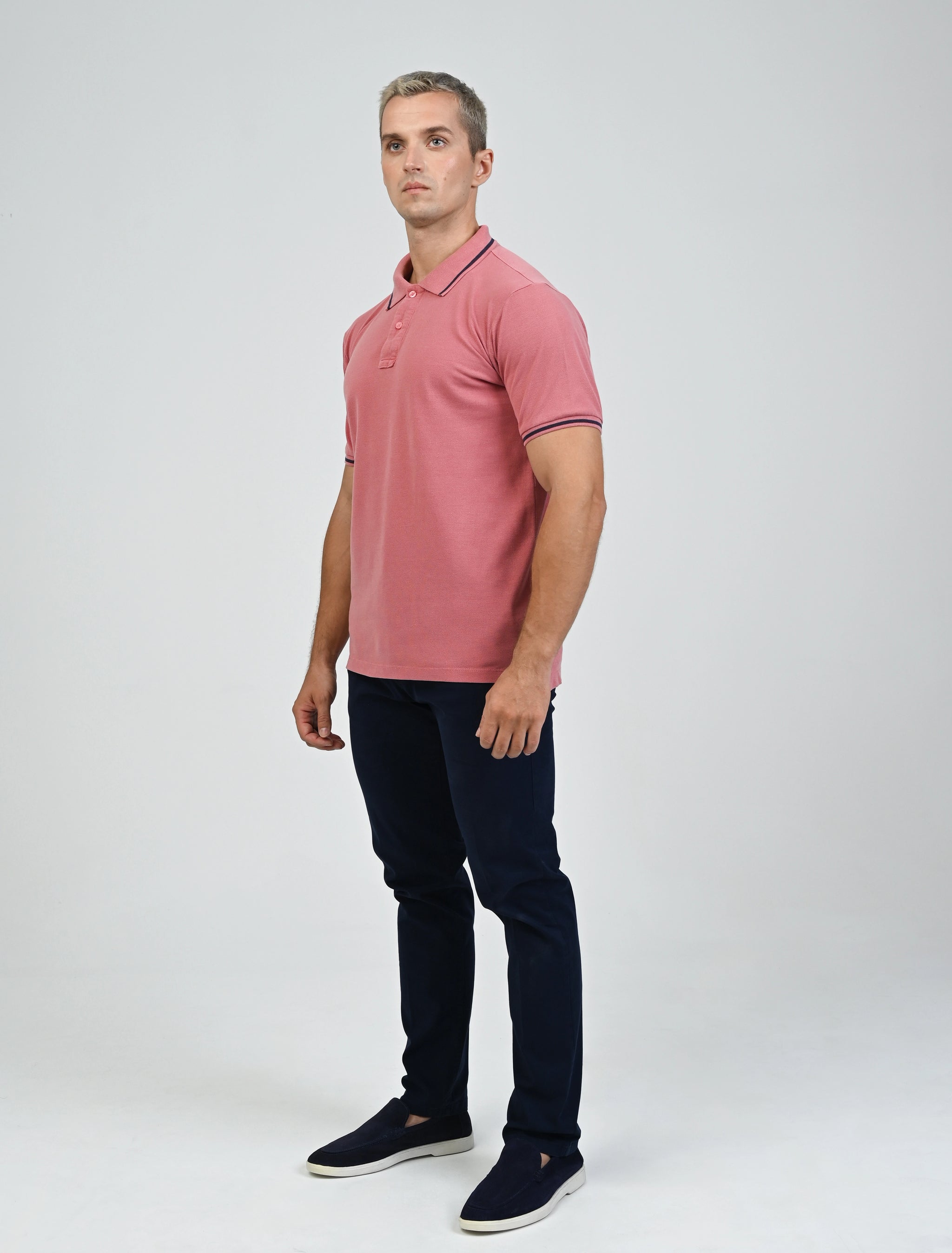 Full-length view of a model wearing the Marshall Menswear Norton Blush Red men's polo shirt with contrast navy tipping, navy chinos and loafers for an elevated smart casual outfit.