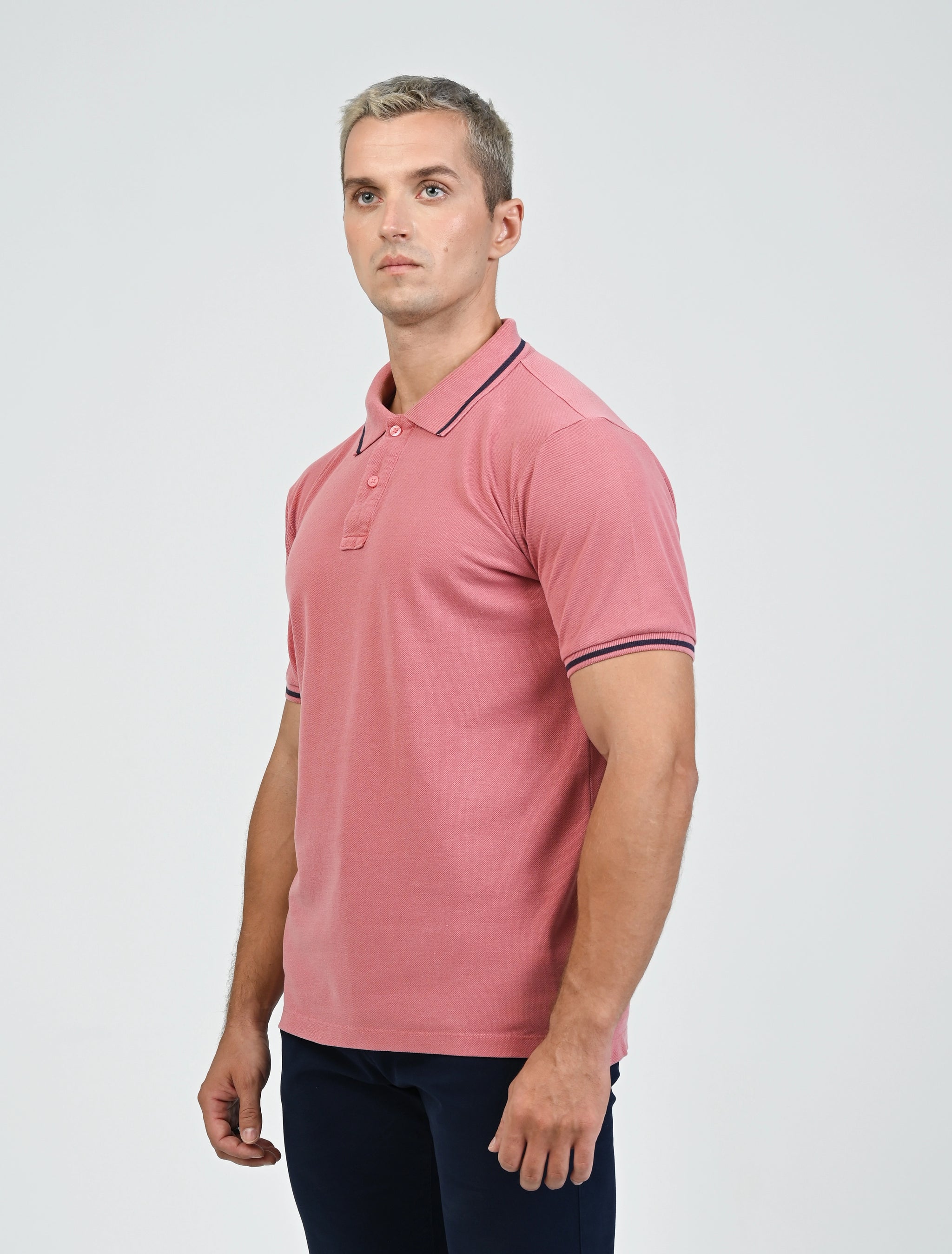 Three-quarter view of the Marshall Menswear Norton Blush Red men's polo shirt showcasing breathable pique fabric, contrast navy tipping, short sleeves and a tailored silhouette.
